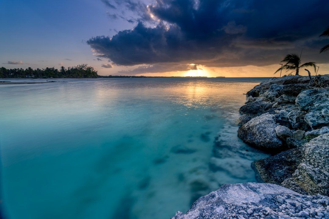 Sunset over calm turquoise water beside a rocky shore